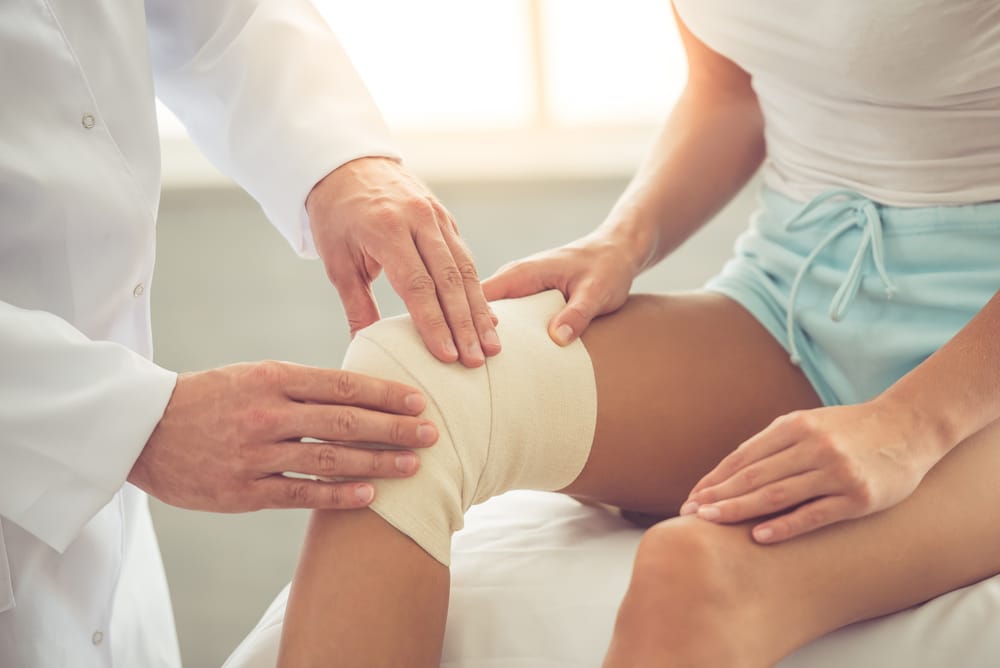 Cropped,Image,Of,Handsome,Doctor,Bandaging,Woman's,Injured,Knee,While