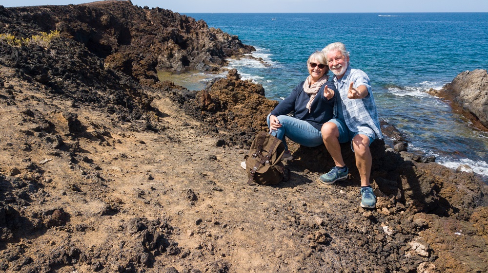 Senior,Caucasian,Couple,White,Hair,Sitting,On,The,Cliff,With